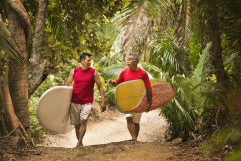 Hispanic men carrying surfboards on jungle trail