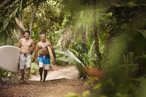 Hispanic men carrying surfboards on jungle trail