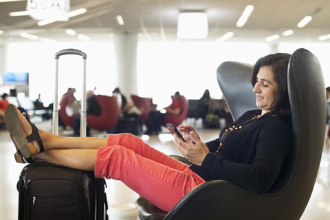Hispanic businesswoman using cell phone in airport waiting area