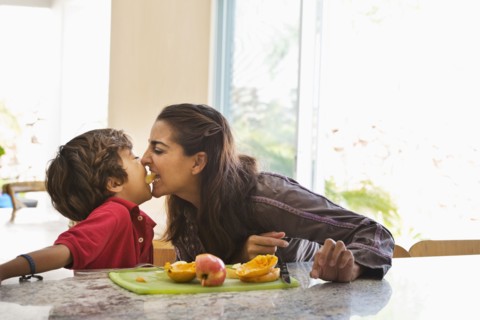 Hispanic mother and son eating fruit in kitchen