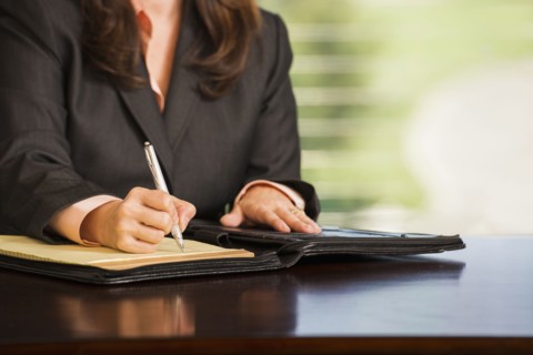 Hispanic businesswoman writing notes at desk