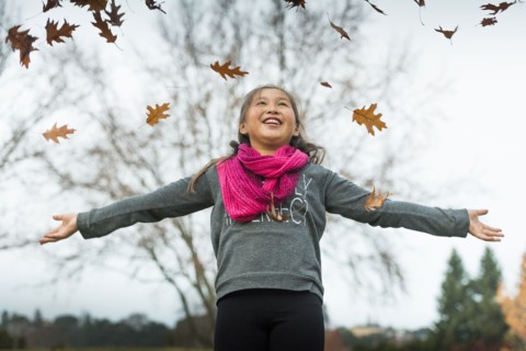 Mixed race girl playing in autumn leaves