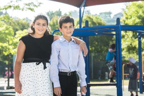 Proud well-dressed Mixed Race brother and sister posing on playground