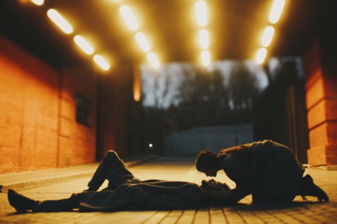 Caucasian woman leaning over man laying on street in tunnel