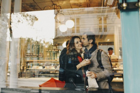 Caucasian man kissing woman on cheek behind bakery window