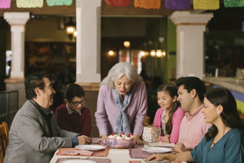 Older woman blowing out candles on birthday cake in restaurant