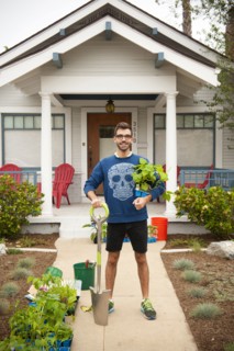 Portrait of smiling Hispanic man holding shovel and plants near house