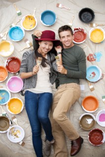 Portrait of couple laying on tarp holding paintbrushes