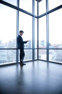 Hispanic businessman leaning on window texting on cell phone