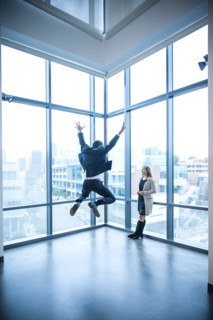 Businesswoman watching businessman celebrating near window