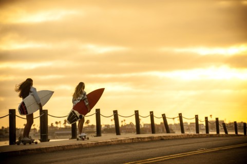 Teenage girls carrying surfboards on skateboards