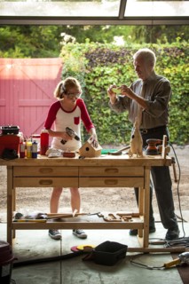 Grandfather photographing granddaughter building birdhouse in garage