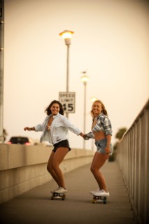 Teenage girls holding hands while riding skateboards