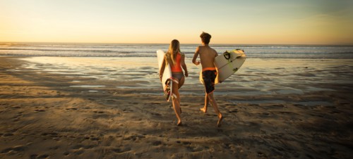 Teenage boy and girl carrying surfboards running to ocean