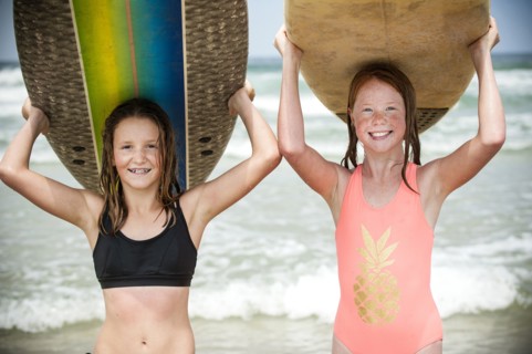 Portrait of smiling girls balancing surfboards on top of heads