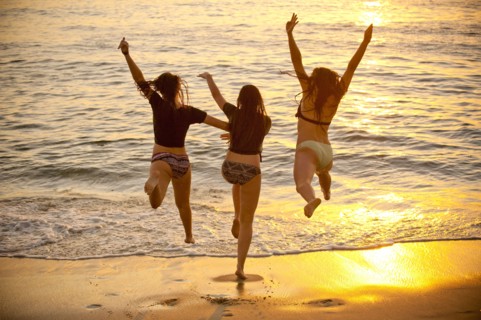 Teenage girls running into ocean at sunset