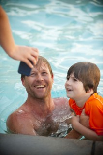 Hand holding cell phone for Caucasian father and son in swimming pool