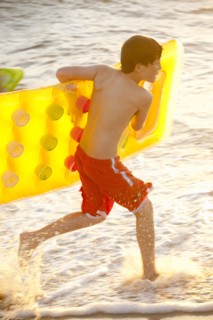 Caucasian boy running into ocean carrying inflatable raft