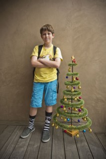 Portrait of Caucasian boy standing near small artificial Christmas tree