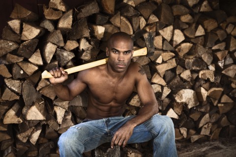 Bare chested African American man near woodpile holding ax