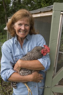 Older Caucasian woman holding chicken near coop