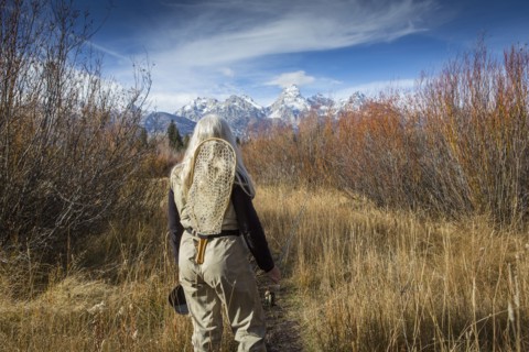 Older Caucasian woman carrying fishing supplies in field