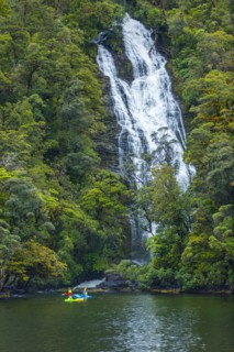 Caucasian friends paddling kayak under remote waterfall