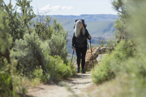 Older Caucasian woman hiking with backpack on path
