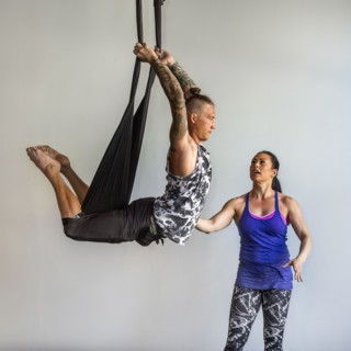 Mixed Race instructor assisting student hanging from silks