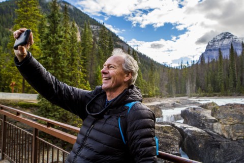Caucasian man posing for cell phone selfie near mountain