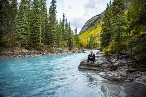 Caucasian woman sitting on rock near mountain river