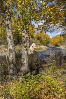 Smiling Caucasian woman leaning on tree near river