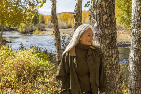 Smiling Caucasian woman leaning on tree near river