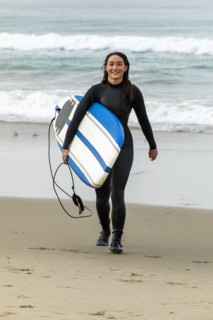 Caucasian woman wearing wetsuit carrying surfboard on beach