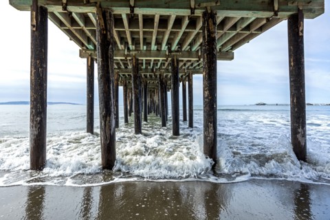 Waves splashing on pilings of wooden pier at beach