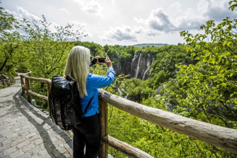 Older Caucasian woman photographing waterfalls with cell phone