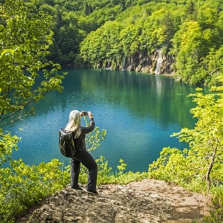 Older Caucasian woman photographing waterfall with cell phone
