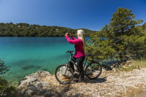 Caucasian woman on bicycle photographing lake with cell phone