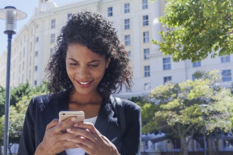 Mixed Race businesswoman texting on cell phone outdoors