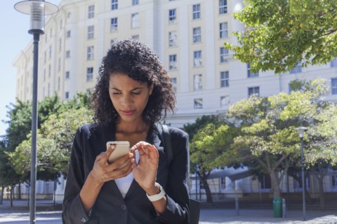 Mixed Race businesswoman texting on cell phone outdoors