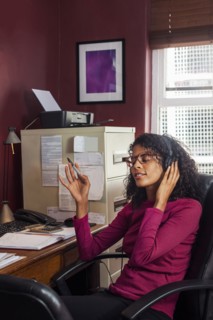 Mixed Race businesswoman listening to headphones in office