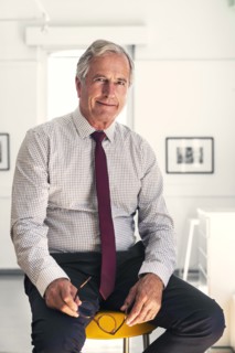 Smiling Caucasian businessman sitting on stool holding eyeglasses