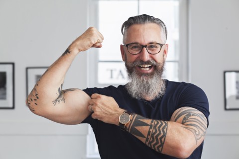 Close up of smiling muscular Caucasian hipster man flexing biceps