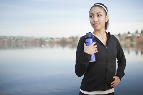 Mixed race woman near lake holding water bottle