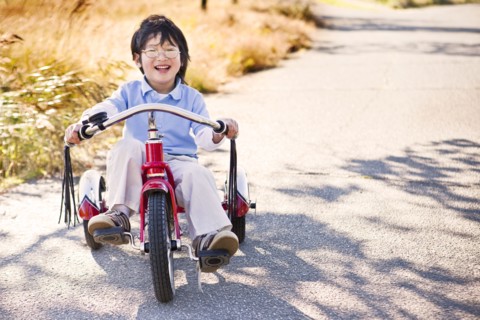 Chinese boy riding tricycle on sidewalk