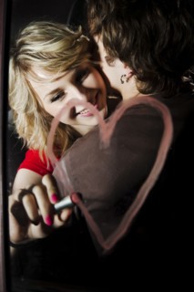 Woman drawing heart with lipstick on mirror while hugging boyfriend