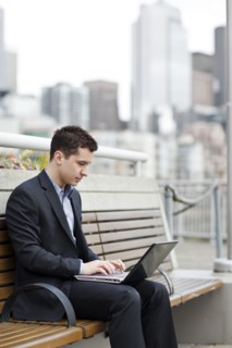 Mixed race businessman using laptop on city bench