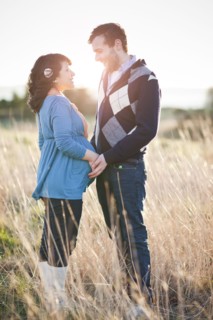 Pregnant woman holding husband's hands in field
