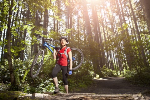 Hispanic woman carrying mountain bike in forest