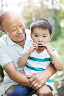 Chinese grandfather watching grandson with harmonica
